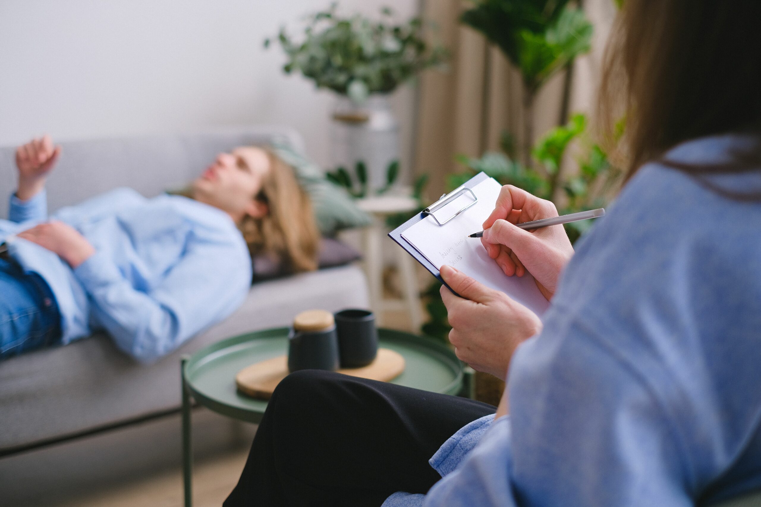 Une personne allongée et détendue sur un canapé pendant qu'une thérapeute prend des notes